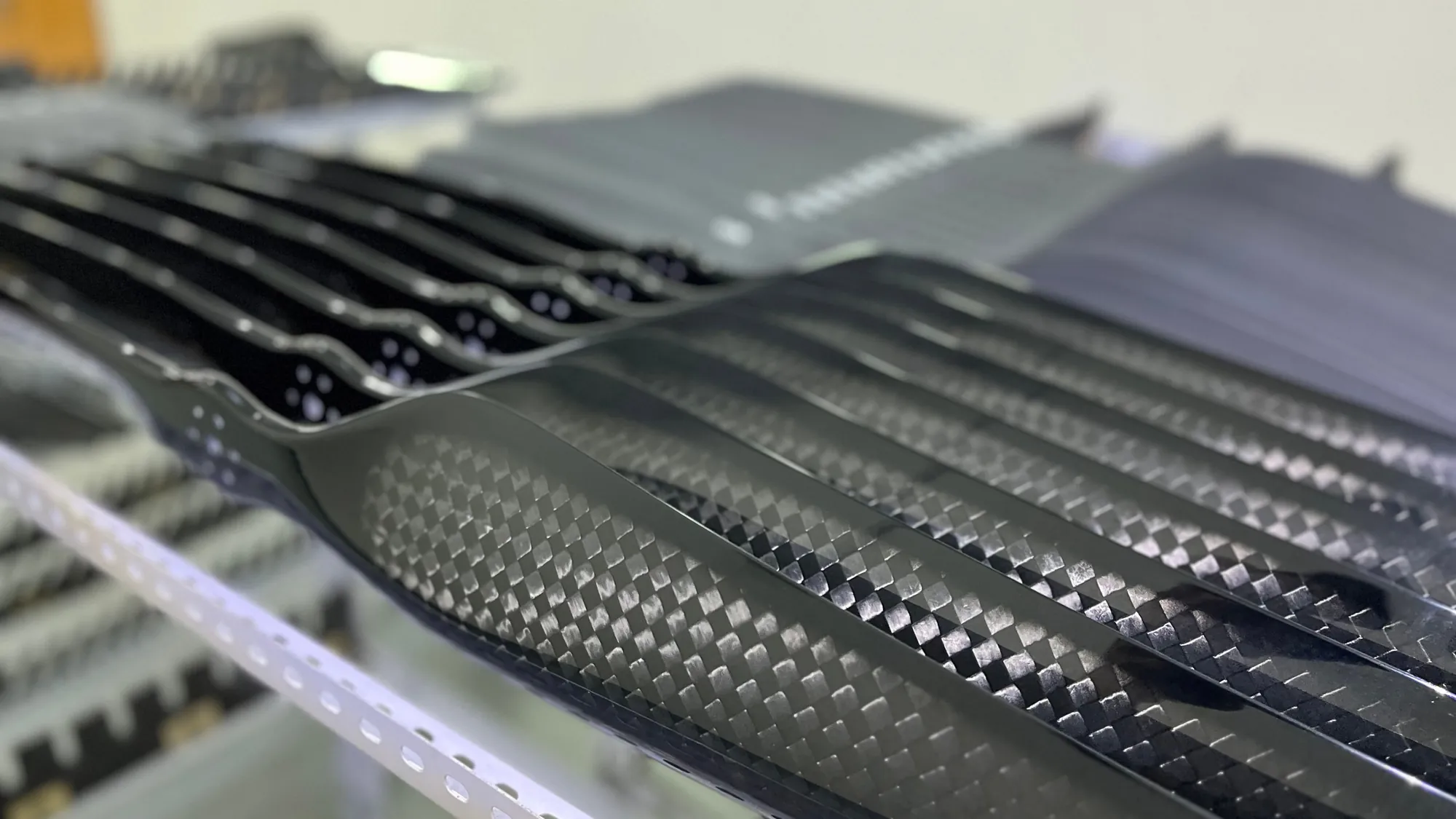 Finished carbon fiber blades racked in rows, the twill weave catching the light