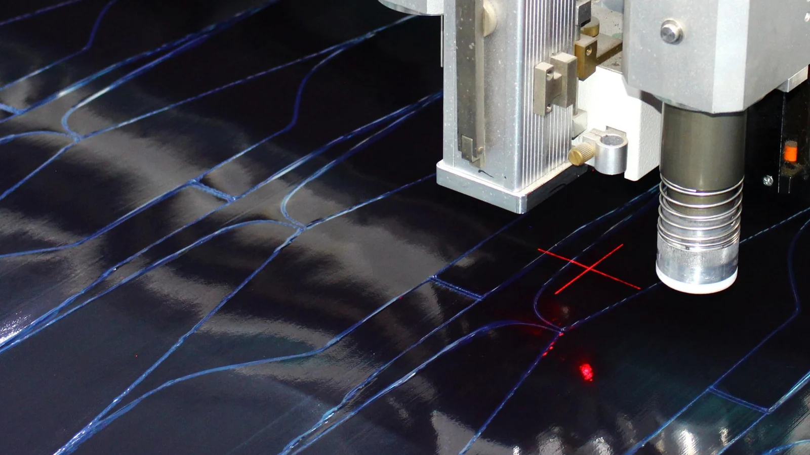 Nested ply outlines and a red laser cross projected on carbon fabric at the cutting table